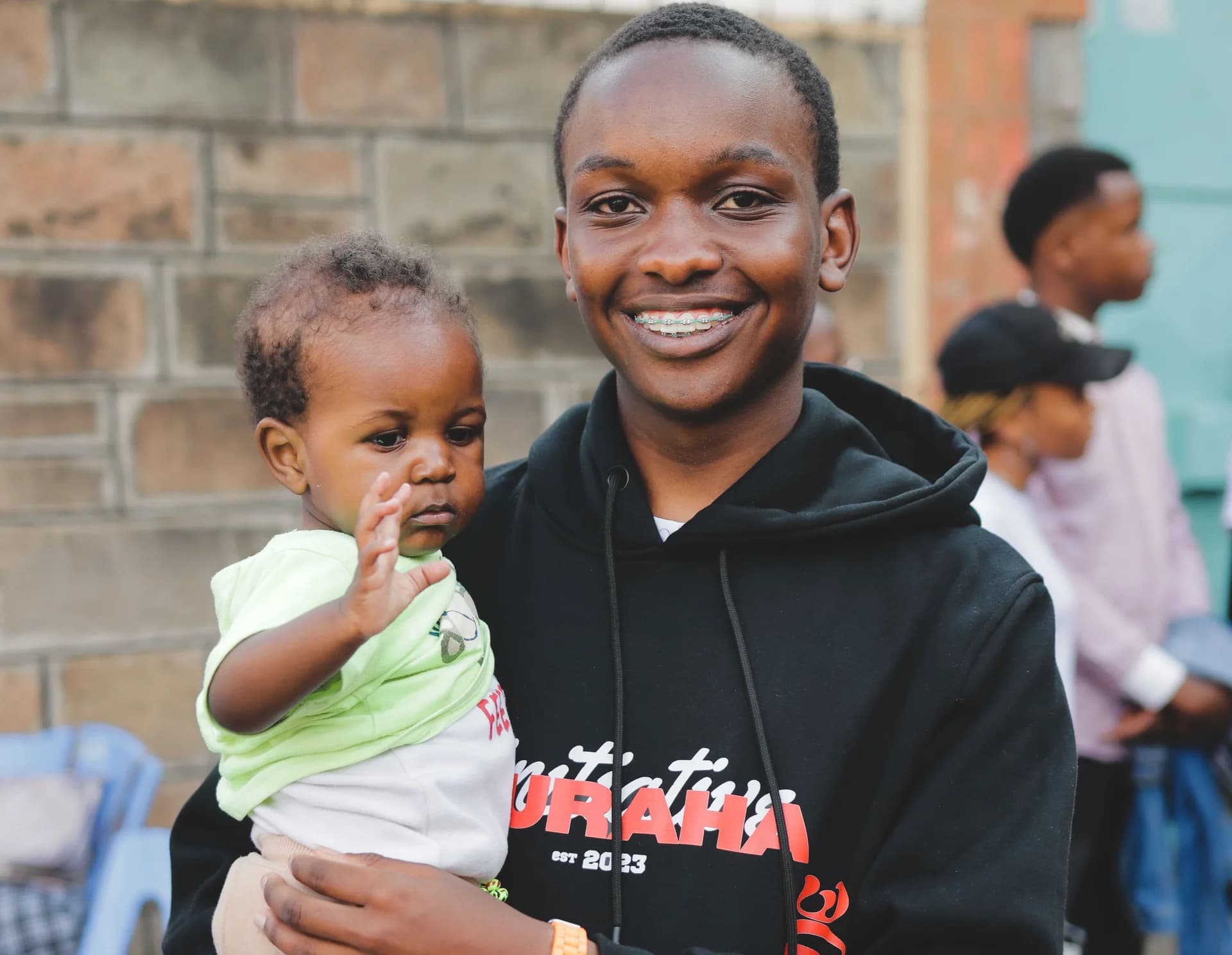 A smiling Furaha volunteer holding a child during a community visit